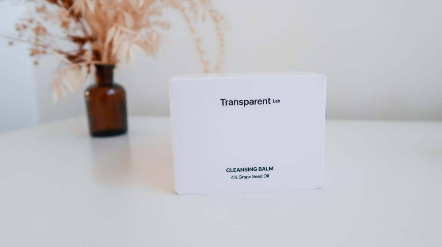Emballage carton noir et blanc de format carr&eacute; du baume d&eacute;maquillant de la gamme Transparent Lab chez Niche Beauty. Derri&egrave;re, un petit vase brun avec des fleurs s&eacute;ch&eacute;es. 